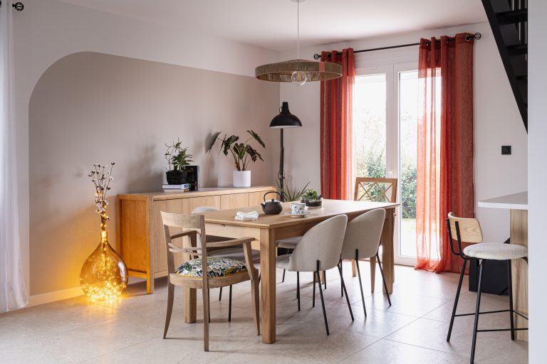Espace salle à manger lumineux avec table en bois, chaises dépareillées et rideaux terracota
